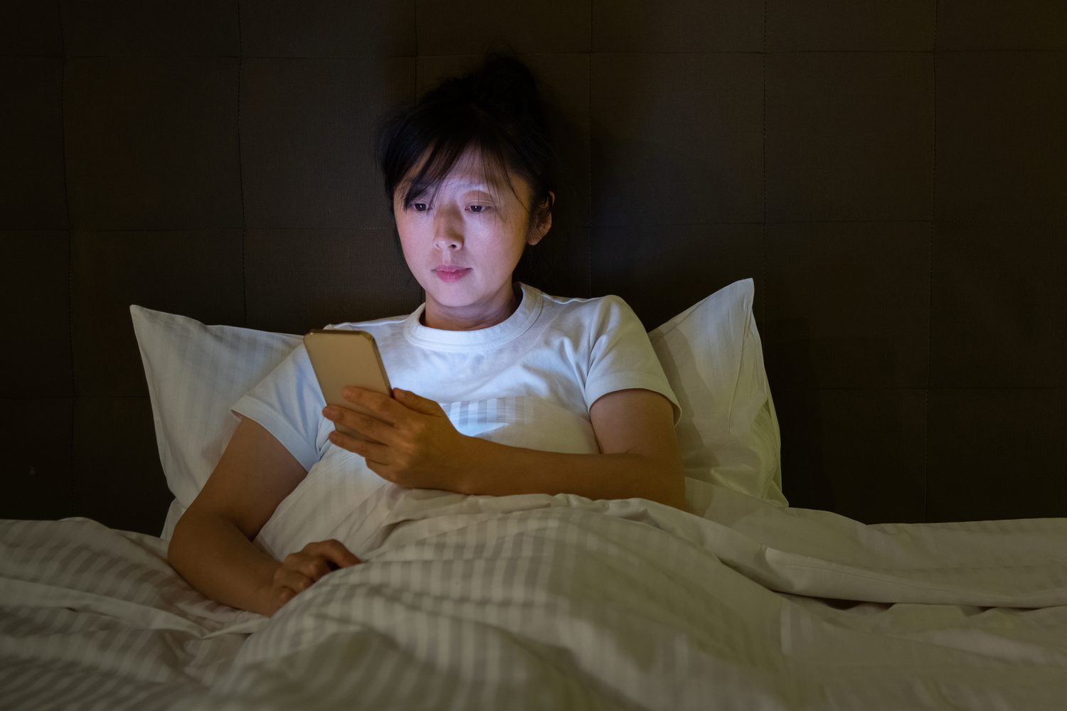 Woman lying in bed at night looking at her smartphone